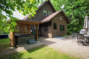 A wooden house with a hot tub, patio chairs, and a covered seating area.