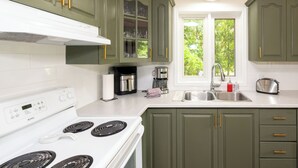 A kitchen with green cabinets, a white stove, and a window with a view of trees. - Cozy Family-Sized Cottage in Kearney - Hot Tub & Sauna 3 Min walk to Perry Lake (Kearney)