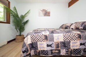 A bedroom with a large bed, a potted plant, a framed picture on the wall, and a window with blinds.