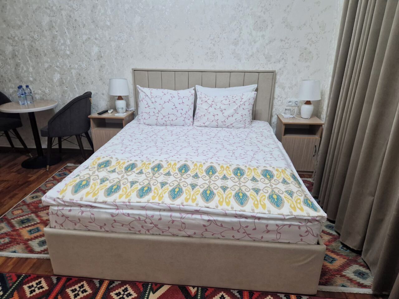 A hotel room with a bed, two bedside tables, a chair, and a small table with a lamp.