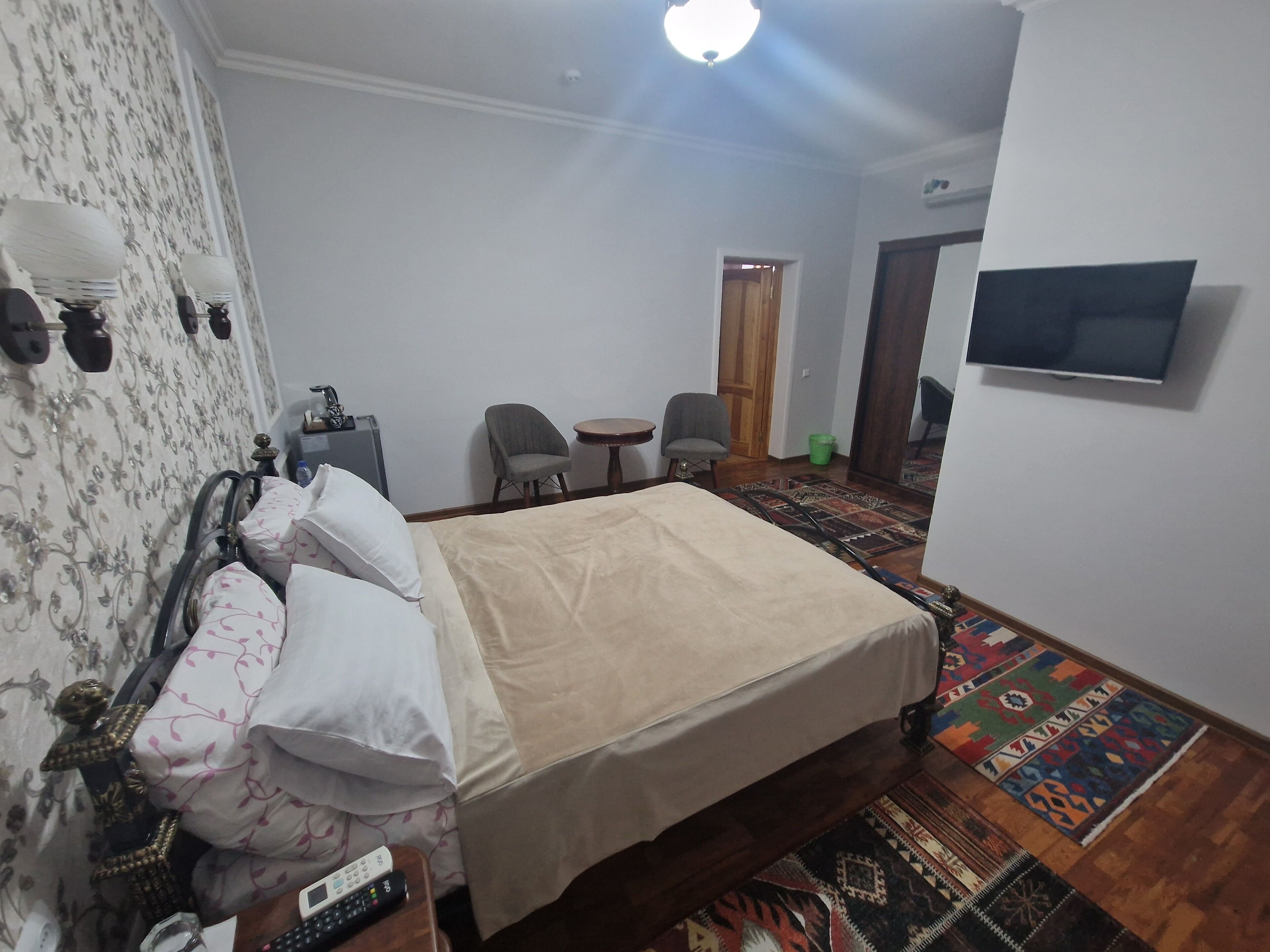 Een hotelkamer met een bed, twee stoelen, een tafeltje, een televisie en een kamerbreed tapijt met dessin.
