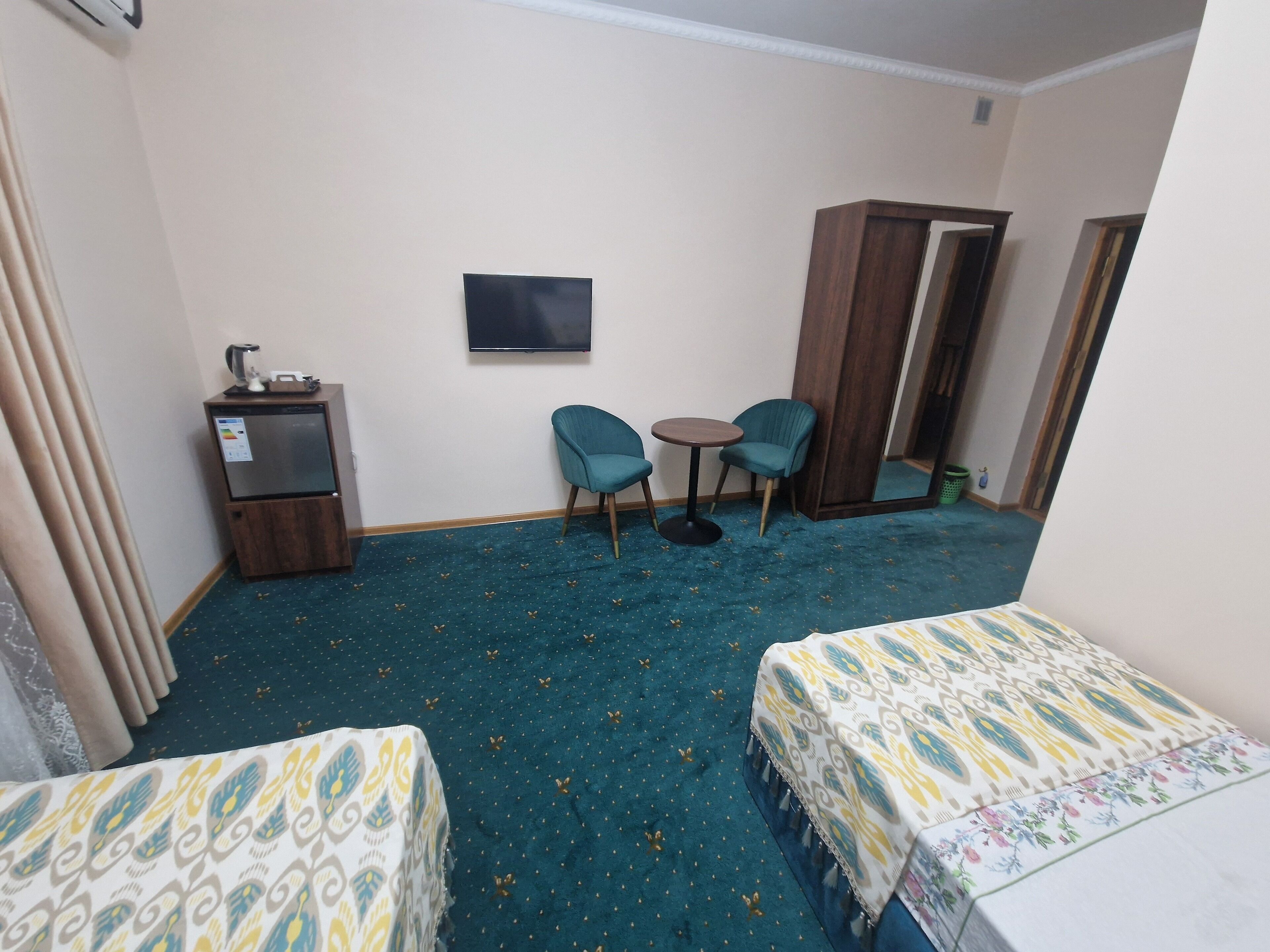 A hotel room with two single beds, a small table, two chairs, a wardrobe, a TV, and a kitchenette.