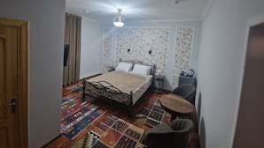 A bedroom with a bed, a small round table, two chairs, a nightstand, and a wall-mounted lamp. - Hotel Kuvonchoy Bonu (Khiva)
