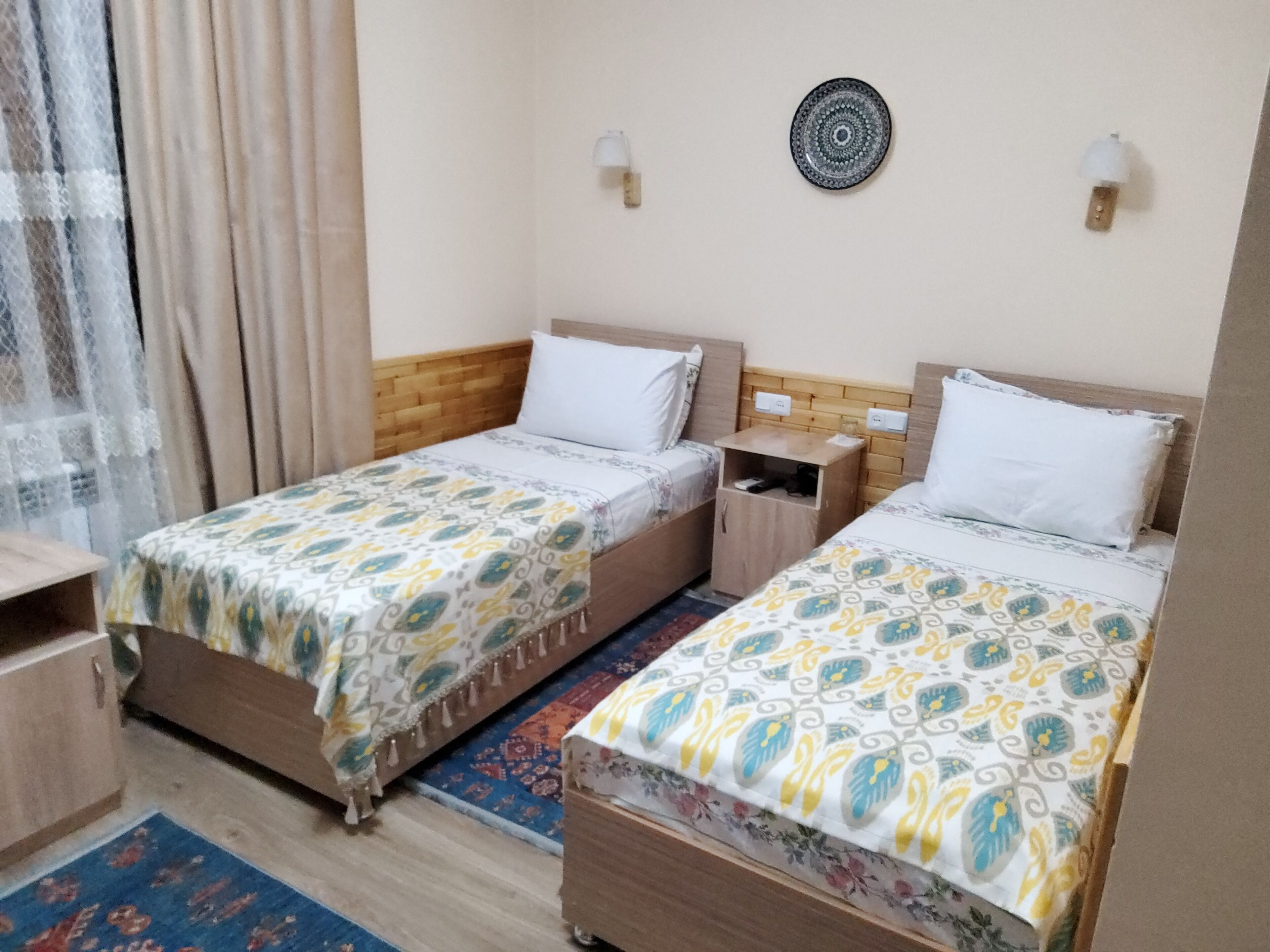 Habitación de hotel con dos camas, una mesita de noche, una lámpara de pared y un plato decorativo.