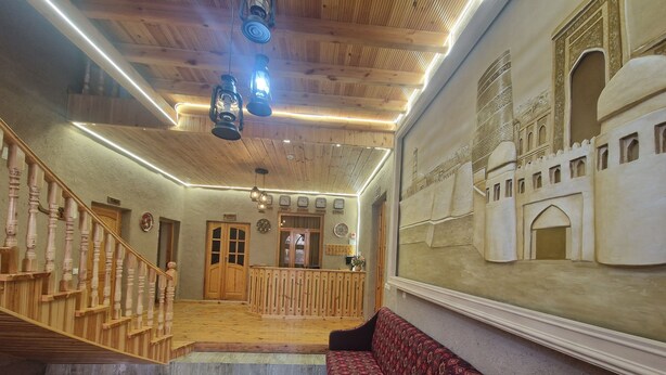 A hotel lobby with a wooden staircase, a reception desk, and a patterned sofa. - Hotel Kuvonchoy Bonu (Khiva)