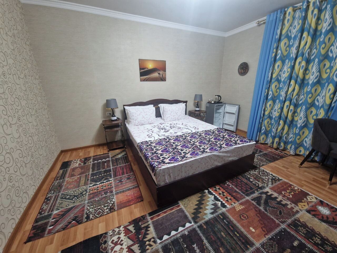 Une chambre à coucher avec un lit, des tapis à motifs, une table de chevet, une lampe et un tableau au mur.