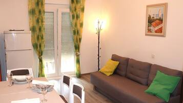 Un salon avec un canapé, une table à manger dressée pour deux personnes et un tableau accroché au mur.