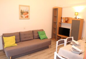 A living room with a sofa, a dining table set for two, a television, and a bookshelf.