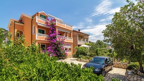 A two-story building with balconies, surrounded by lush greenery and a parked car. - Apartment mit Meerblick (Barbat)