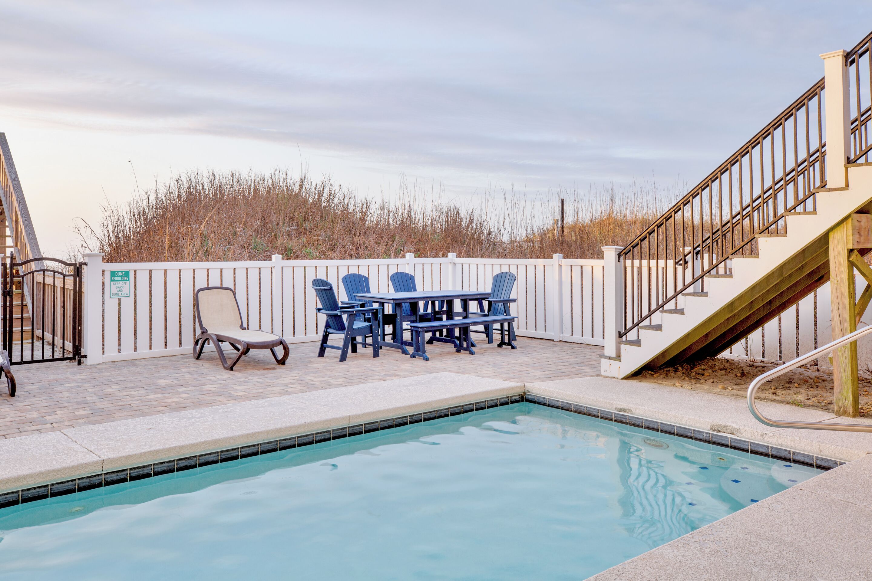 A swimming pool with a table and chairs, a wooden deck, and a staircase leading to an upper level.