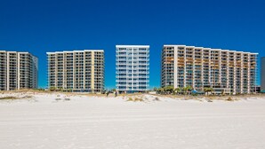 A beachfront hotel with multiple high-rise buildings, sandy beach in the foreground, and clear blue sky. - Perdido Dunes Tower 9e 4 Bedroom Condo (Orange Beach)