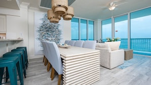 A modern kitchen with a dining area, large windows, and a view of the ocean. - Perdido Dunes Tower 9e 4 Bedroom Condo (Orange Beach)