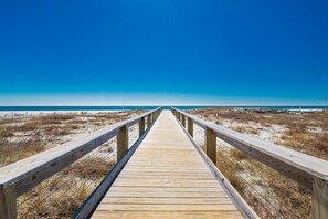 Une promenade en bois qui mène à une plage, avec un ciel bleu dégagé.