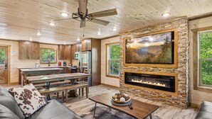 A spacious living area with a fireplace, wooden ceiling, and a large TV mounted on a stone wall.