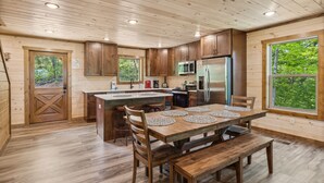A wooden cabin kitchen with a central island, wooden cabinets, and a large window offering a view of the forest.
