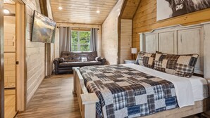 A wooden cabin bedroom with a bed, a sofa, and a painting of a bull.
