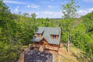 A cabin with a green roof, wooden exterior, and a porch with a bench. - Hilltop Dreamin' 4 Bedroom Cabin by RedAwning (Sevierville)