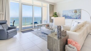 Un moderno salón con vista al océano, un sofá, un sillón, una mesa de centro y una lámpara.