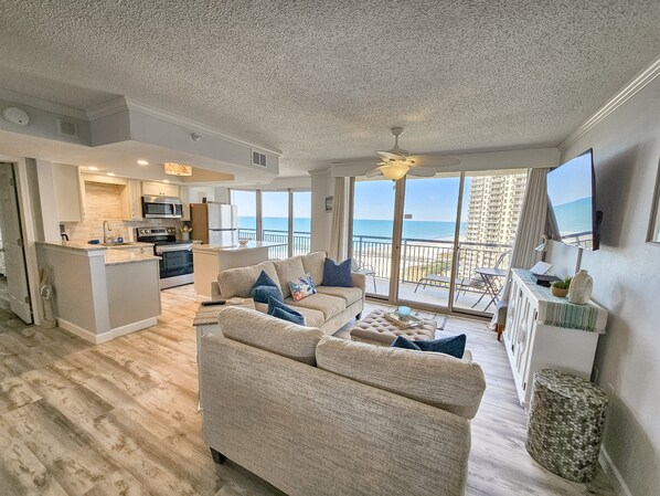 A spacious living area with a large sofa, a coffee table, and a view of the ocean through large windows. - Oceanview Condo In Brighton, 1504 - Full Access 2 Bedroom Condo (Myrtle Beach)