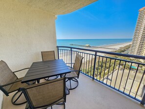A balcony with a table and chairs, overlooking a beach and a high-rise building. - Oceanview Condo In Brighton, 1504 - Full Access 2 Bedroom Condo (Myrtle Beach)