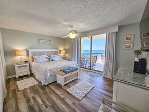 A bedroom with a bed, nightstands, a ceiling fan, a view of the ocean through large sliding doors, and a balcony with outdoor furniture. - Oceanview Condo In Brighton, 1504 - Full Access 2 Bedroom Condo (Myrtle Beach)