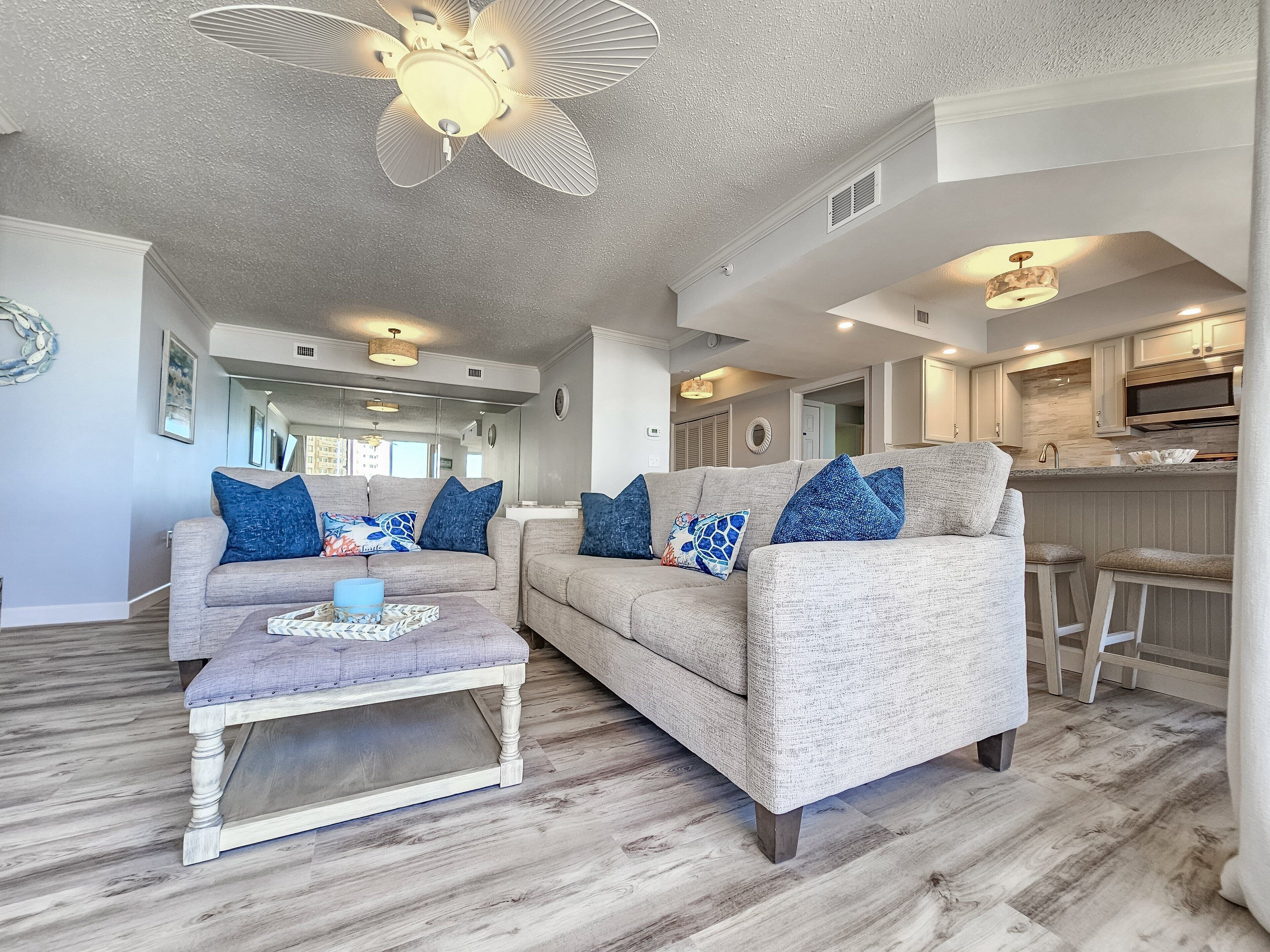 A spacious living room with a grey sofa set, a coffee table, and a ceiling fan.