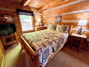 Een slaapkamer in een blokhut met een bed, een televisie, een raam en een bordje aan de muur.