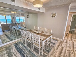 A dining area with a glass partition, a wooden table, and white chairs. - Oceanview condo in Brighton, 1504 - full access (Myrtle Beach)