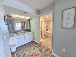 A bathroom with a wooden vanity, a large mirror, a sink, and a shower. - Oceanview condo in Brighton, 1504 - full access (Myrtle Beach)