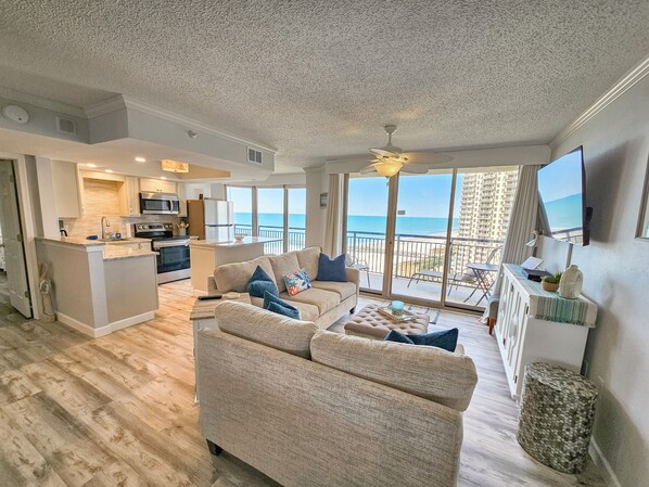 A spacious living area with a sofa and a coffee table, a kitchen with a central island, and a balcony with a view of the ocean. - Oceanview condo in Brighton, 1504 - full access (Myrtle Beach)