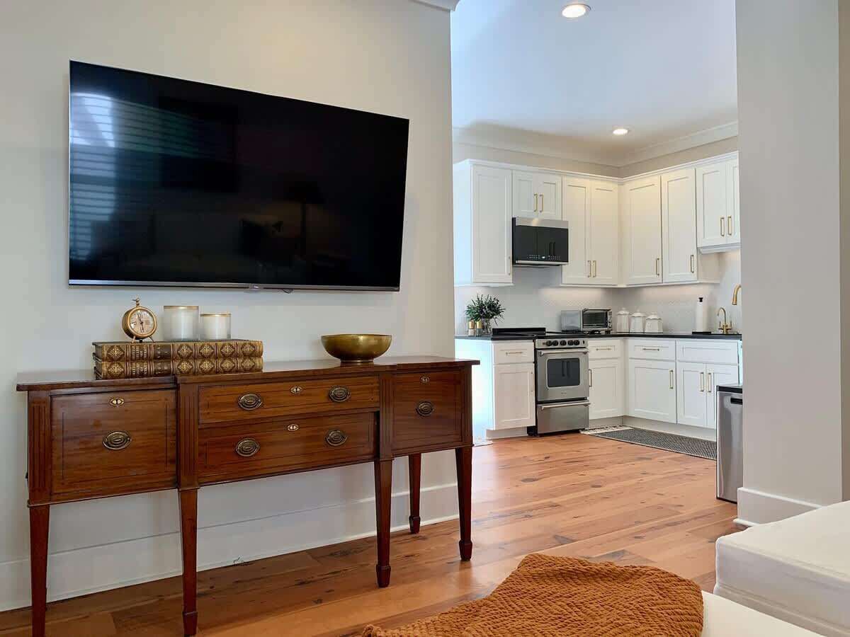 A modern kitchen with white cabinets, a flat-screen TV, a wooden dining table with drawers, and a kitchen island.