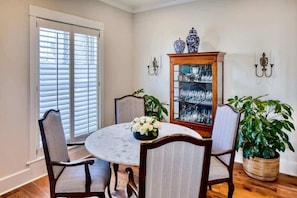 A dining area with a round table, four chairs, a cabinet with glassware, and two wall sconces. - The Shain Manor Garden Suite (Savannah)