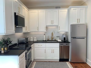 A modern kitchen with white cabinetry, stainless steel appliances, and a black countertop. - The Shain Manor Garden Suite (Savannah)