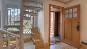A staircase with a wooden finish, a wooden door with a glass panel, and a view of the outside through a window.