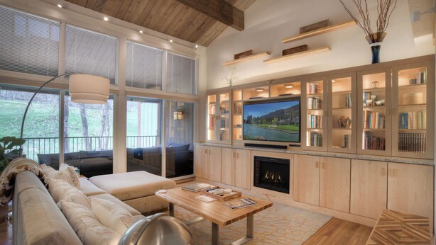 A modern living room with a large TV, wooden bookshelves, a fireplace, and a cozy seating area.