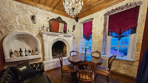 Ein Zimmer mit Steinwand, Kamin, einer Chandelüster, einem Esstisch mit Stühlen und einem Ledersofa.