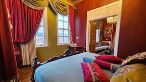 Ein Zimmer mit einem großen Bett, roten Vorhängen, einem Holzkopfende und einem Spiegel an der Wand.
