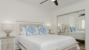 Un dormitorio con cama, mesitas de noche, ventilador de techo y un espejo grande.