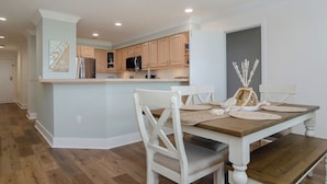 Una cocina moderna con armarios de madera, una isla central y un comedor con mesa de madera y sillas blancas.