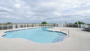 Una piscina rectangular con muelle blanco y barandillas de metal, rodeada por una valla blanca.