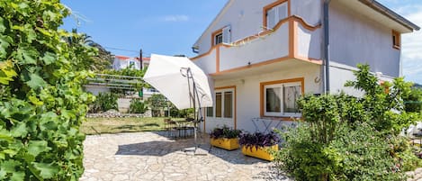 Una casa de dos pisos con un patio de piedra, mobiliario exterior y plantas en macetas.