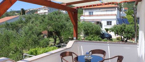 An outdoor patio with a table and chairs, a white umbrella, and a view of a residential area with houses and trees.