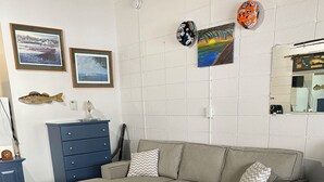 A modern bedroom with a grey sectional sofa, a striped bed, wooden flooring, a blue dresser, and wall-mounted decorations including framed pictures and a fish sculpture.