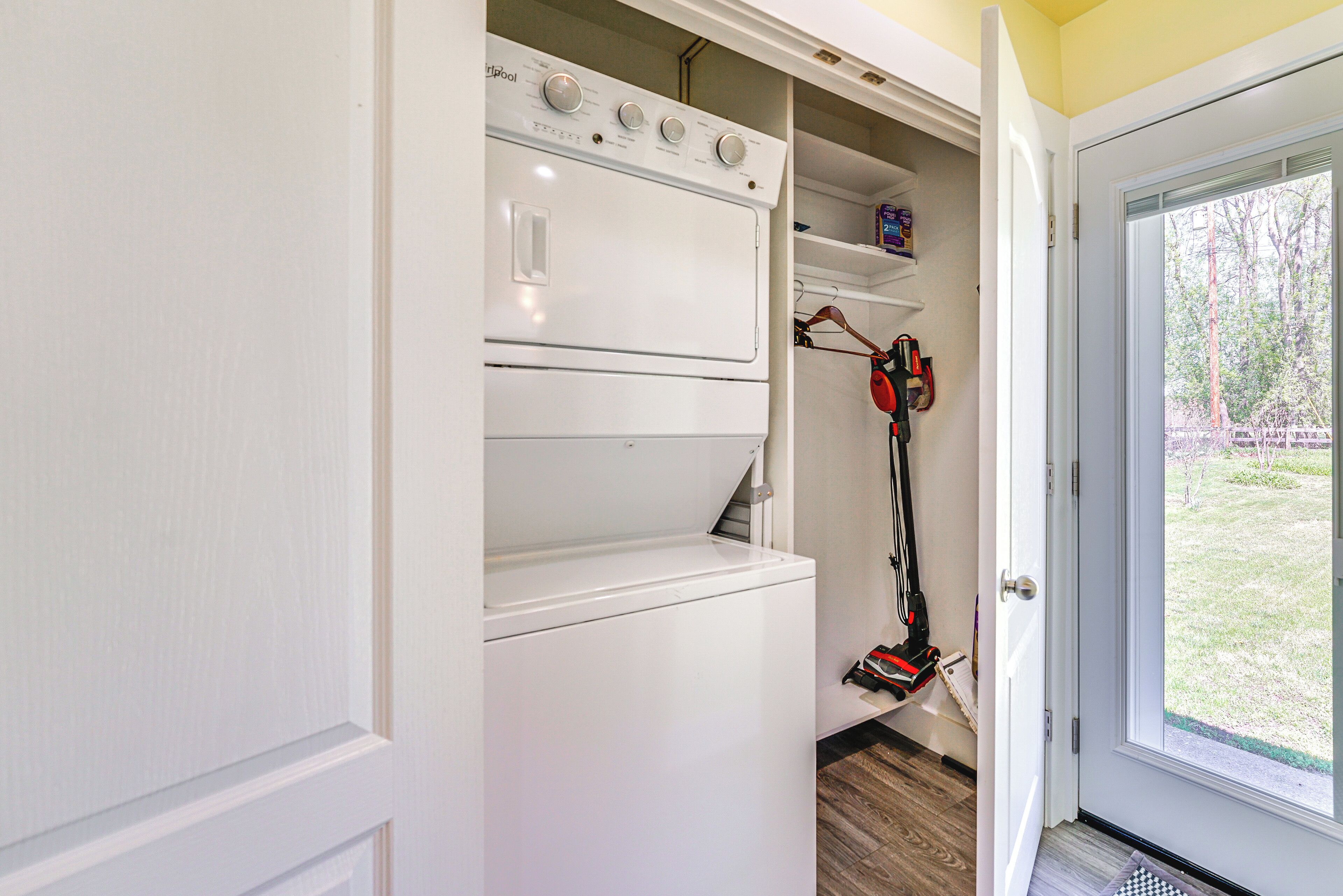 A laundry room with a front-loading washer and dryer, a shelf with cleaning supplies, and a vacuum cleaner.