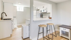 A modern kitchen with white cabinets, a microwave, and a small refrigerator. There are two wooden stools and a small table. - San Diego Apartment w/ Patio - Near Balboa Park! (San Diego)