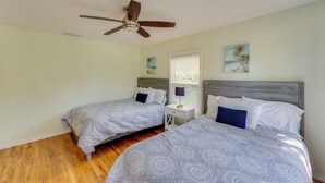 A bedroom with two beds, a ceiling fan, a nightstand, and a window with blinds.