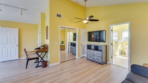 A spacious living room with hardwood flooring, a ceiling fan, a flat-screen TV, and a dining area with a table and chairs.