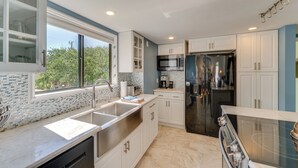 A modern kitchen with white cabinets, a stainless steel sink, a built-in oven, and a large window.