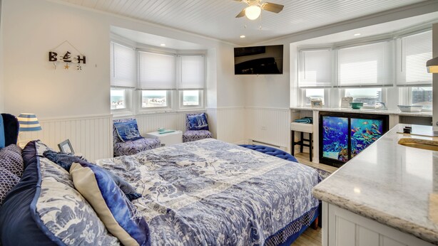 A bedroom with a large bed, a ceiling fan, and a view of the city through the windows. - Ocean City Hideaway: Walk to Boardwalk & Beach! (Ocean City)