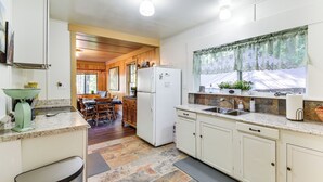 A kitchen with white cabinets, a refrigerator, a sink, and a window with a lace curtain.